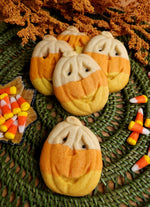 Jack-o-lantern molded pumpkin cookies in candy corn colors on a green woven mat with candy corn colors