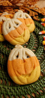 Molded jack-o-lantern pumpkin cookies in candy corn colors on a textured surface with candy corn in the background.