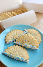 Decorated Artesao Cookie molded daisy cookies with sprinkles on a blue plate, with more cookies in the background.