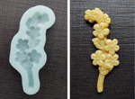 An unbaked cookie in the shape of a single stem of flowers and leaves next to the Artesao Silicone Cookie Mold used to create it
