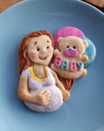 Cookie of a pregnant woman holding a teddy bear balloon with 'BABY' on a blue plate.
