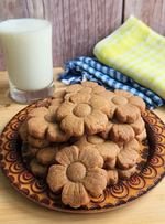 Flower-shaped cookies on a plate with a glass of milk and a towel in the background.